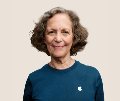 Apple Retail employee with shoulder-length hair and a necklace, smiling at the camera.