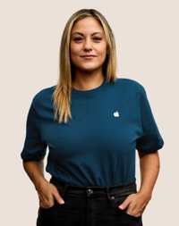Apple Retail employee with shoulder-length hair, smiling at the camera.