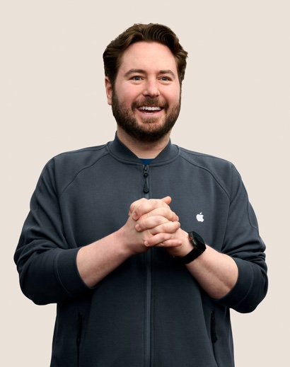 Apple Retail employee with shoulder-length curly hair, smiling at the camera.