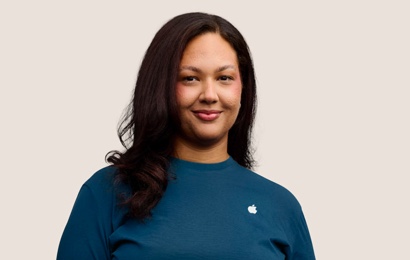 Apple Retail employee with curly hair, looking into the camera.