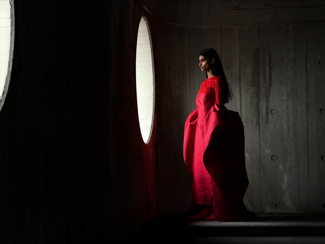 Femme portant une longue robe rouge photographiée dans une pièce vide. L’app Photos montre les distances focales pour illustrer les capacités du système caméra Pro : 100 mm