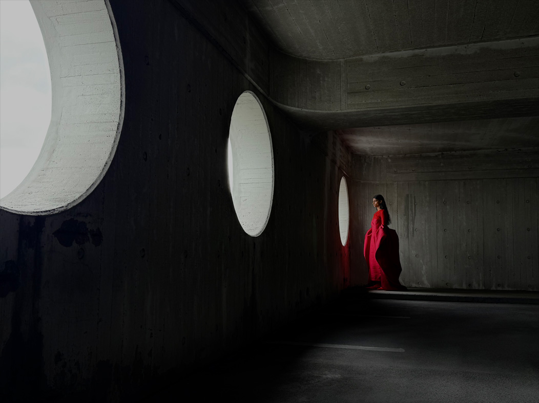 Femme portant une longue robe rouge photographiée dans une pièce vide. L’app Photos montre les distances focales pour illustrer les capacités du système caméra Pro : 35 mm