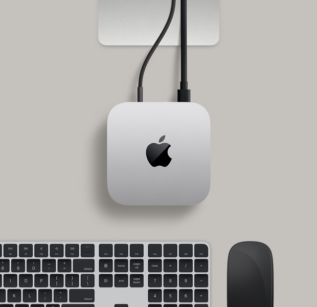 Vedere de sus a unui Mac mini argintiu, cu două cabluri conectate de la porturile din spate la un monitor, alături de Magic Mouse și Magic Keyboard negre