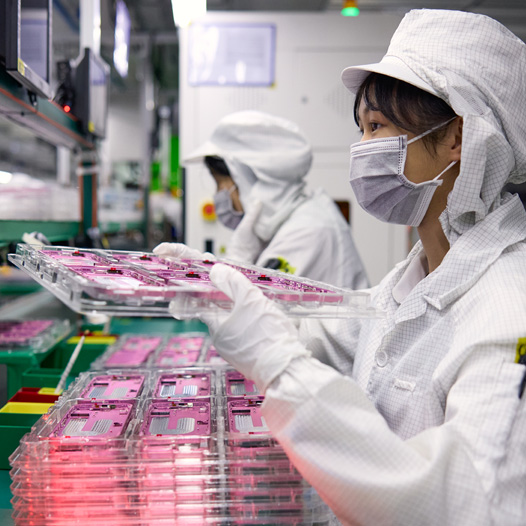 موظفتان مرتديتان زيّ عمل يغطي كامل الجسم تتعاملان مع أجزاء iPhone في منشأة تجميع